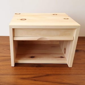 Könnte beinhalten: Ein Nachttisch aus hellem Holz mit einer Schublade und einem Regal. Der Nachttisch ist aus Naturholz mit einer hellen Oberfläche.