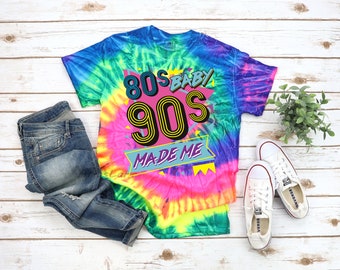 May include: A tie-dye t-shirt with the text "80s Baby 90s Made Me" in a retro font. The shirt is a vibrant neon rainbow color.