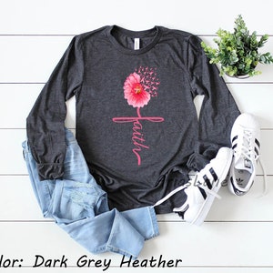 May include: A long-sleeved shirt in dark grey heather with a pink flower design and the word "faith" written in pink script. The flower is made up of pink ribbons.