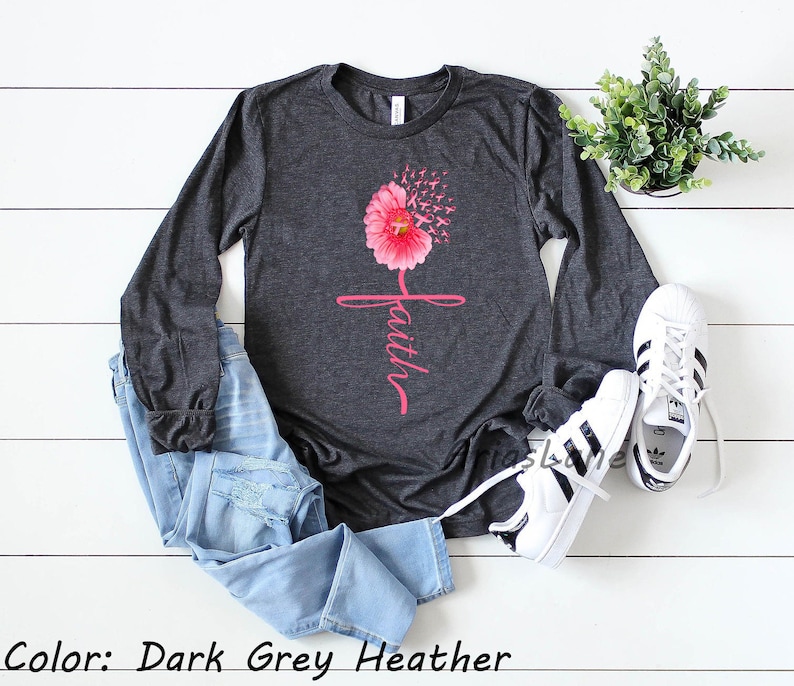 May include: A long-sleeved shirt in dark grey heather with a pink flower design and the word "faith" written in pink script. The flower is made up of pink ribbons.