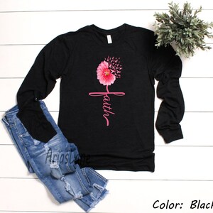 May include: Black long-sleeved shirt featuring a pink flower design and the word "faith" written vertically. The flower is made up of pink ribbons.