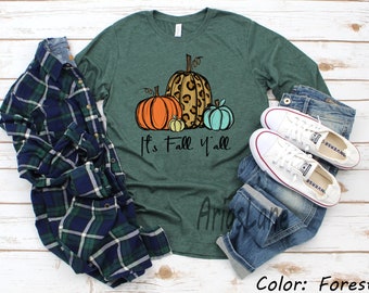 May include: A green long-sleeved t-shirt with the text "It's Fall Y'all" and a graphic of three pumpkins. One pumpkin is orange, one is yellow, and one is teal with a leopard print design.