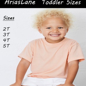 May include: A young child wearing a peach coloured t-shirt and white shorts. The child is smiling and has blonde curly hair. The text "Sizes" is written in black at the top of the image, followed by a list of sizes: 2T, 3T, 4T, 5T.