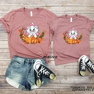 May include: Two mauve t-shirts with a cartoon white cat wearing a pink bow sitting in a pumpkin patch. The text "SHIRTS SOLD SEPARATELY" is at the bottom of the image.