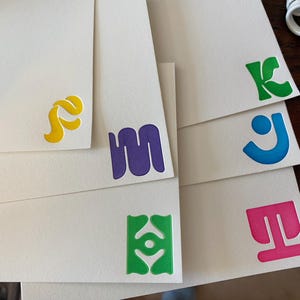 Könnte beinhalten: Ein Satz von sechs leeren Karten mit bunten, abstrakten Designs. Die Designs beinhalten einen gelben Wirbel, eine lila Kringel, eine grüne augenartige Form, ein rosafarbenes T-förmiges Design, ein blaues J-förmiges Design und ein grünes K-förmiges Design.