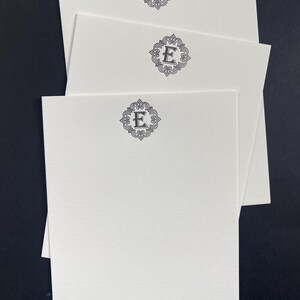 May include: Three white note cards with a decorative black monogram of the letter "E" on each card.