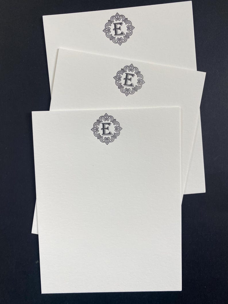 May include: Three white note cards with a decorative black monogram of the letter "E" on each card.