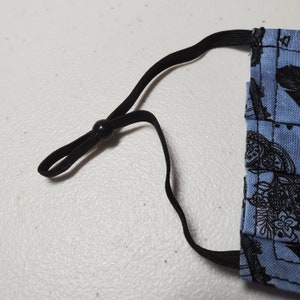 May include: Black elastic ear loops with a black toggle on a blue fabric face mask with a black and white pattern.