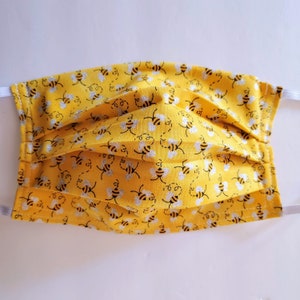 May include: Yellow face mask with a repeating pattern of black and white bees. The mask has white elastic ear loops.