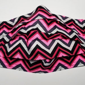 Könnte beinhalten: Eine Gesichtsmaske mit Chevron-Muster in Pink, Schwarz und Weiß mit elastischen Ohrschlaufen.