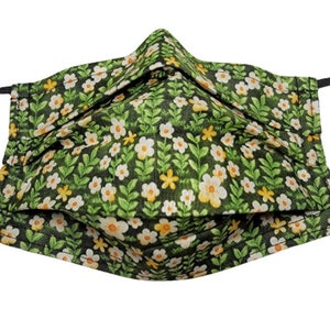 May include: A green fabric face mask with a white and yellow floral pattern. The mask has black elastic ear loops.
