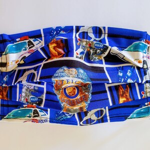 May include: Blue face mask with a repeating pattern of police cars, badges, and handcuffs. The mask has black elastic straps.
