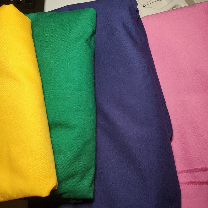 May include: Four fabric swatches in different colors: yellow, green, blue, and pink. The swatches are folded and arranged in a row.