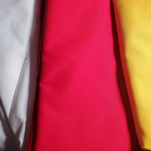 May include: Three fabric swatches in white, red, and yellow. The swatches are folded and arranged side by side.
