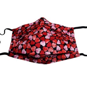 May include: A black face mask with a red and pink heart pattern. The mask is pleated and has adjustable ear loops.