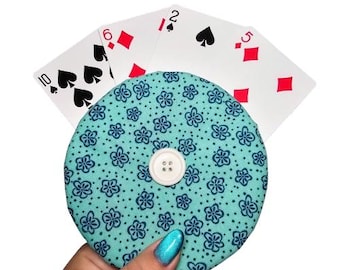 May include: A teal blue fabric coin purse with a white button and a floral pattern. The purse is holding a stack of playing cards, including the 10 of spades, 6 of diamonds, 2 of spades, and 5 of diamonds.