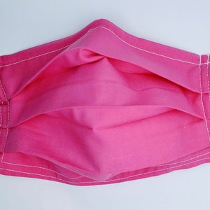 May include: A pink face mask with white stitching. The mask is pleated and has elastic ear loops.