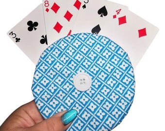 May include: A blue and white fabric circle with a white button in the center. The circle is surrounded by playing cards with red and black suits.