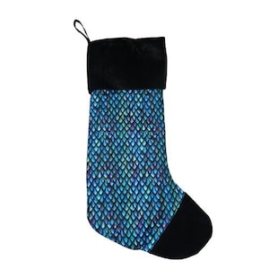 Könnte beinhalten: Ein Weihnachtsstrumpf mit schwarzem Bündchen und Spitze. Der Körper des Strumpfes weist ein blaues, türkisfarbenes und violettes Schuppenmuster auf. Eine schwarze Schlaufe ist zum Aufhängen angebracht. Der Strumpf ist für die Weihnachtsdekoration gedacht.