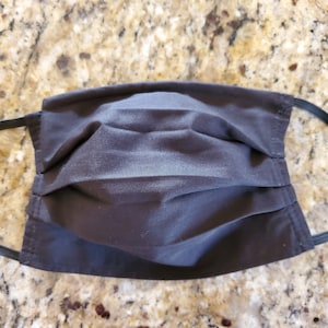 May include: A black cloth face mask with pleats and elastic ear loops.