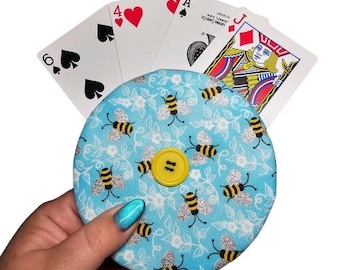 May include: A blue and white fabric coin purse with a yellow button and a bee pattern. The purse is decorated with silver glitter.