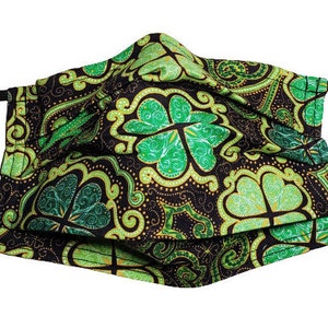 May include: A black face mask with a green and gold shamrock pattern. The mask is made of fabric and has elastic ear loops.