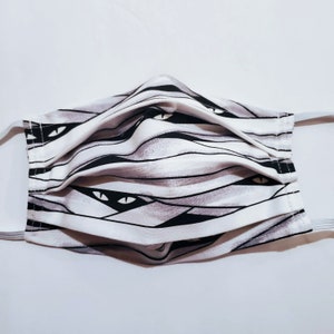 May include: White face mask with a black and gray mummy pattern. The pattern features bandages and eyes.