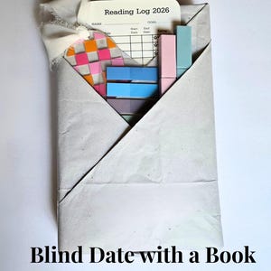 May include: A gray paper envelope containing a reading log, colorful sticky notes, and a decorative bookmark. The reading log is labeled "Reading Log 2026". The text "Blind Date with a Book Surprise Gift Set" is at the bottom.