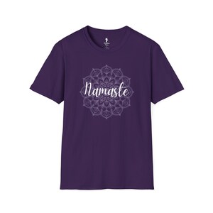 May include: A purple t-shirt featuring a white mandala design with the word "Namaste" in a cursive font. The shirt has short sleeves and a crew neck. The design is centered on the front of the shirt.