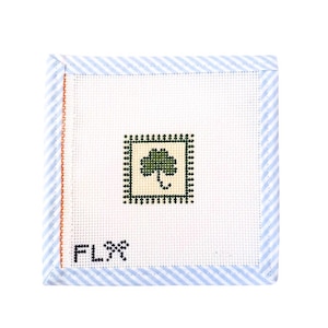 Può includere: Tela per punto croce quadrata con sfondo bianco, bordo a righe blu e bianco e un motivo a trifoglio verde. Le lettere "FL" e un simbolo sono cuciti in nero.