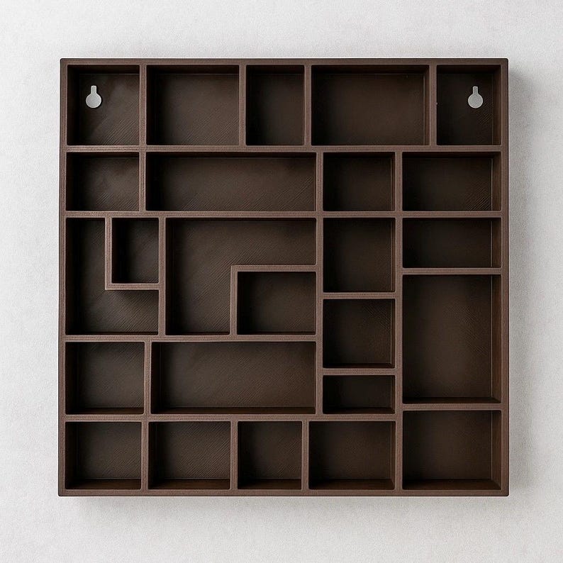 May include: A dark brown, square wall shelf with a geometric design. The shelf features a variety of cubby sizes and shapes, perfect for displaying small items. Two keyhole hangers are visible on the back for easy mounting. The shelf is approximately 61 cm wide.