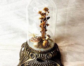 Diorama de cúpula de cristal vintage con base de metal ornamentada, setas, flores secas y mariposas.