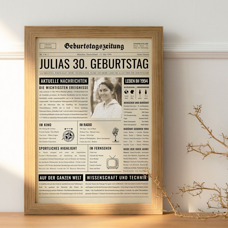 May include: A framed print designed to look like a vintage newspaper, with the headline "JULIAS 30. GEBURTSTAG." The print includes sections on news, sports, and entertainment, with a photo of a woman. The frame is made of light-colored wood.