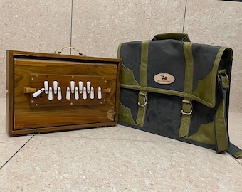 May include: A wooden harmonium with white keys and a dark brown finish, next to a black and green canvas bag with a leather strap and a brown leather patch with a logo.