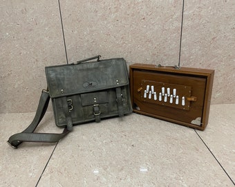May include: A dark gray leather briefcase with a shoulder strap and a wooden harmonium with white keys.