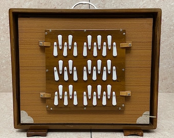May include: A wooden box with a hinged front panel. The panel is open, revealing a grid of white plastic keys. The box has a brown wood finish and a metal handle on the top.