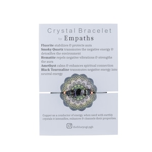 May include: A crystal bracelet for empaths with a mandala design. The bracelet features fluorite, smoky quartz, hematite, amethyst, and black tourmaline crystals. The text on the card reads: "Crystal Bracelet for Empaths. Fluorite stabilizes & protects aura. Smoky Quartz transmutes the negative energy & detoxifies the environment. Hematite repels negative vibrations & strengths the aura. Amethyst calms & enhances spiritual connection. Black Tourmaline transmutes negative energy into neutral energy. Copper as a conductor of energy, when used with earthly crystals it intensifies, enhances & channels their properties. theblueyogi.pgh"