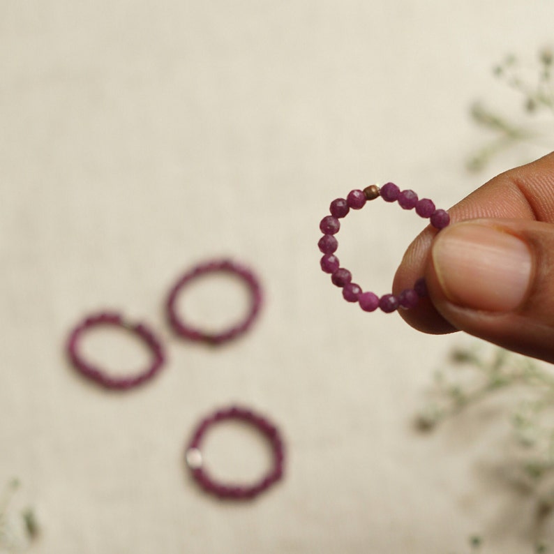 K&ouml;nnte beinhalten: Drei violette Perlenringe mit einem goldenen Perlenakzent. Die Ringe bestehen aus kleinen, facettierten Perlen.