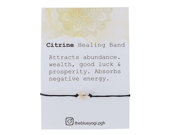 May include: Citrine Healing Band bracelet with black string and a small citrine stone. The card reads "Citrine Healing Band Attracts abundance. wealth, good luck & prosperity. Absorbs negative energy." and includes the Instagram handle "theblueyogi.pgh".