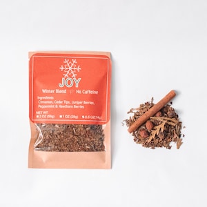 May include: A small, orange and white pouch with a snowflake design and the word "JOY" printed on it. The pouch contains a blend of dried herbs and spices, including cinnamon, cedar tips, juniper berries, peppermint, and hawthorn berries. The pouch is labeled "Winter Blend" and "No Caffeine". The pouch is also labeled with the net weight of the contents: 2 oz (56g), 1 oz (28g), and 0.5 oz (14g).
