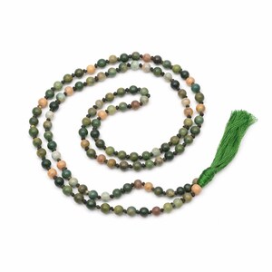 May include: A long beaded necklace with a green tassel. The beads are a mix of green, brown, and tan colors. The necklace is made of small, round beads strung together on a black cord. The tassel is a bright green color.