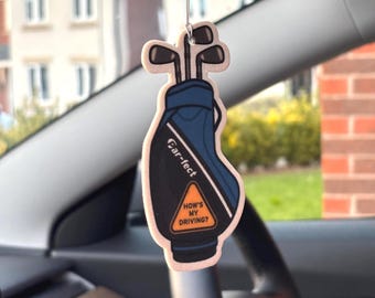 Può includere: Un deodorante per auto da appendere a forma di sacca da golf blu e nera contenente diverse mazze da golf. La sacca presenta la scritta "Ear-fect" e un segnale triangolare giallo con il testo nero "HOW'S MY DRIVING?" stampato sul davanti.