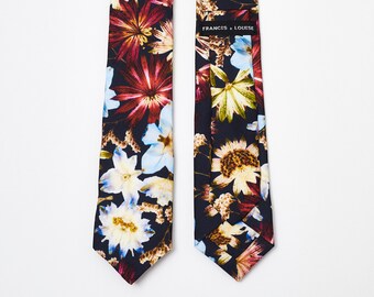 May include: A dark blue necktie with a floral print featuring red, yellow, and blue flowers. The tie has a label that reads "FRANCIS + LOUISE".