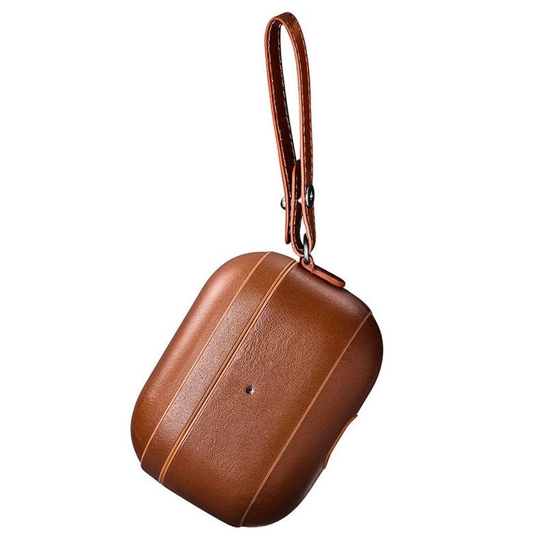 May include: A brown leather protective case for wireless earbuds featuring a smooth, textured finish with vertical stitched detailing and a matching brown leather wrist strap attached to a metal ring at the top of the rectangular enclosure.