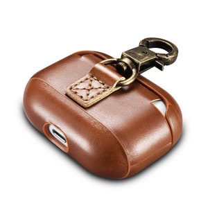 May include: A brown leather protective case for wireless earbuds featuring a smooth finish, a cutout for a charging port, and a stitched leather tab attached to a dark metallic bronze-toned swivel lobster clasp hook for secure attachment.