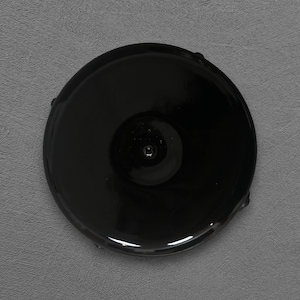 Może przedstawiać: Błyszczący, czarny, okrągły przedmiot z centralnym wklęśnięciem i małym, wypukłym detalem. Obiekt ma gładką, odblaskową powierzchnię. Ogólny kształt to idealne koło.