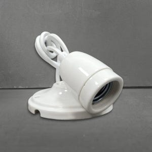 Op de afbeelding: Een witte keramische lampfitting met een lamphouder en een ronde basis. Een wit snoer is bevestigd aan de fitting. De fitting is ontworpen voor plafond- of wandmontage.