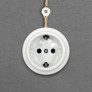 Peut inclure: Une prise électrique ronde blanche avec trois trous et deux broches métalliques. La prise est fixée sur un mur gris et reliée à un cordon beige. La prise est de style vintage.
