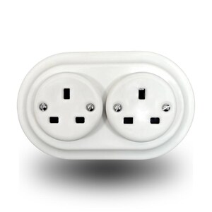 Può includere: Una presa elettrica a muro doppia di colore bianco con una placca frontale ovale e arrotondata. L'unità presenta due prese circolari, ciascuna dotata di tre fessure rettangolari e due piccole viti di montaggio argentate sui lati.