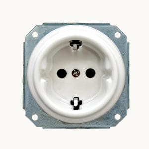 Op de afbeelding: Een wit, rond elektrisch stopcontact met een glanzende afwerking, voorzien van twee ronde openingen en twee metalen aardingsklemmen aan de boven- en onderkant. Het stopcontact is gemonteerd op een vierkant frame van gegalvaniseerd staal met vier gaten.